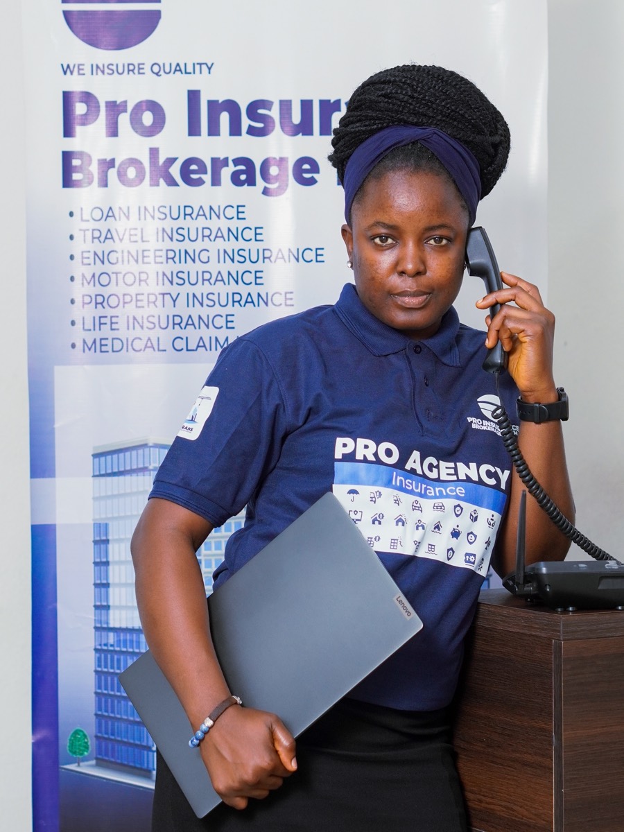 A Pro-Insurance adviser taking a client call beside the firm's banner listing the classes of insurance it arranges